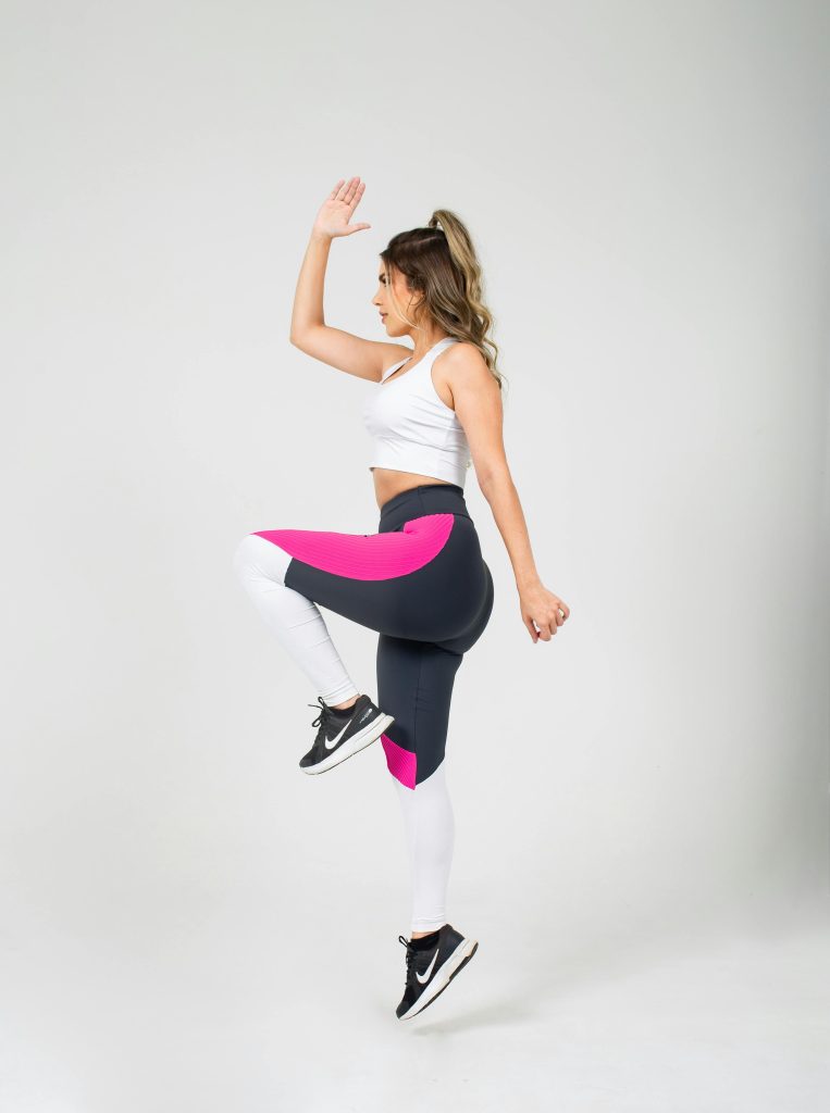 Dynamic studio shot of a woman in colorful sportswear performing a high knee exercise.